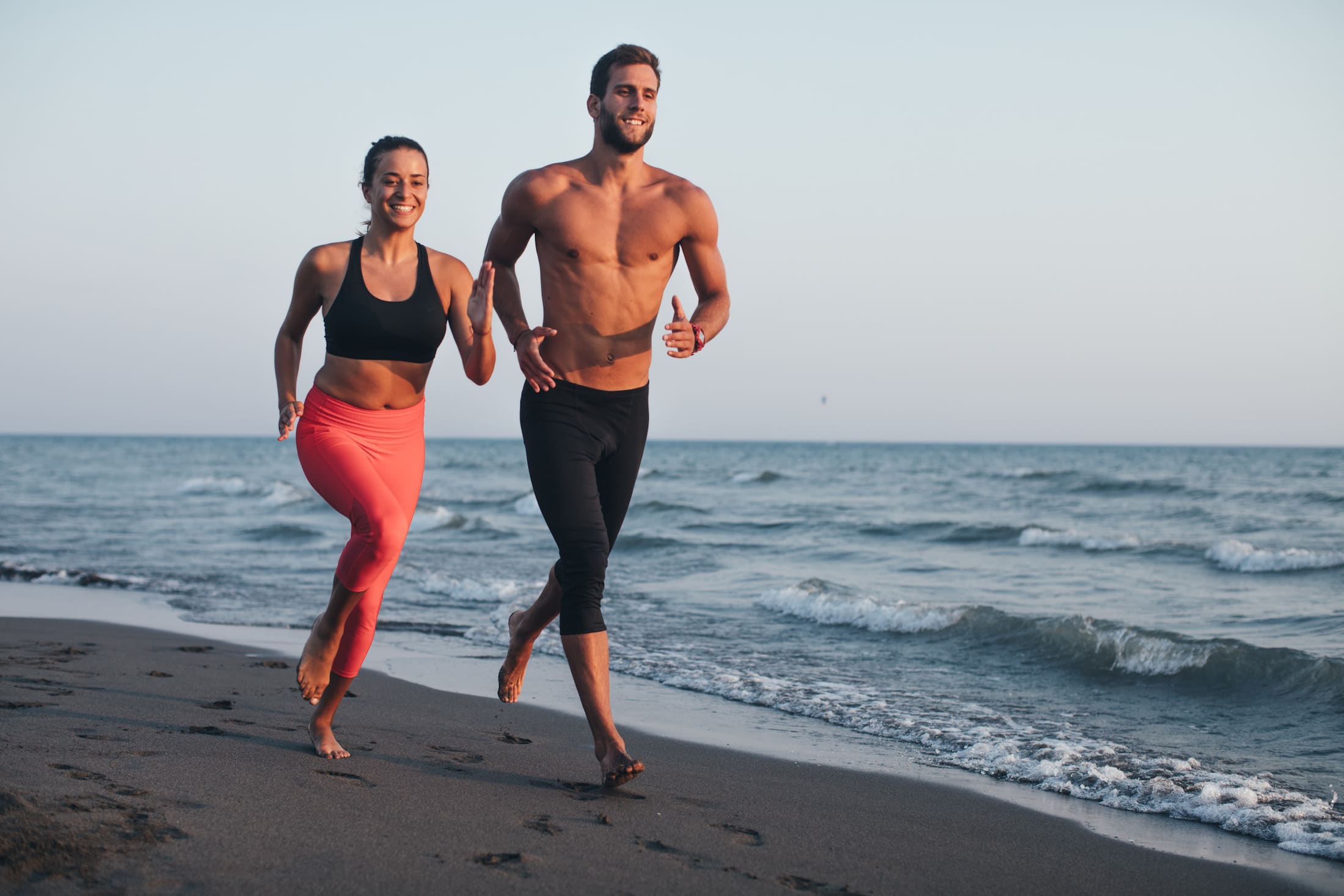 Woman and man jogging on the beach in workout clothes