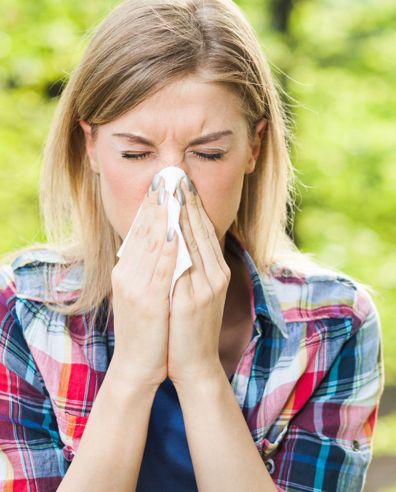 Blonde woman blowing her nose into a tissue